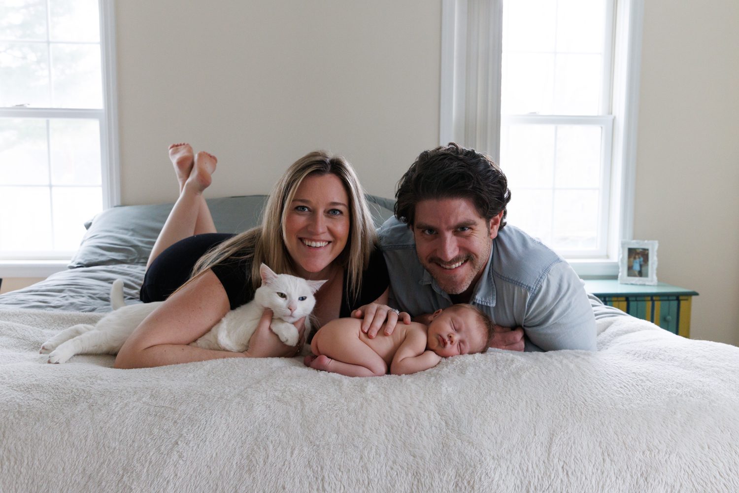 Cute couple on bed laying with their newborn baby and white cat
