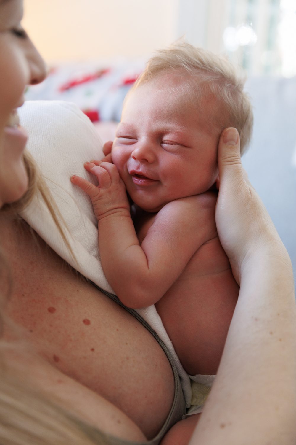 smiling newborn with eyes closed in Mom's arms as she holds, feeds and smiles back down on him