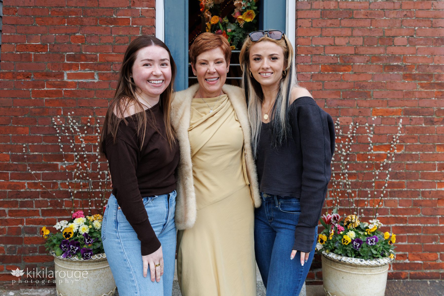 Gorgoeus redheaded woman in golden dress with fur shawl with two younger women on either side in jeans