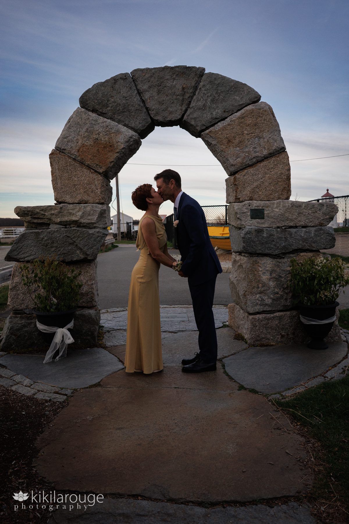 Couple in silhouette in front of a stone archway kissing