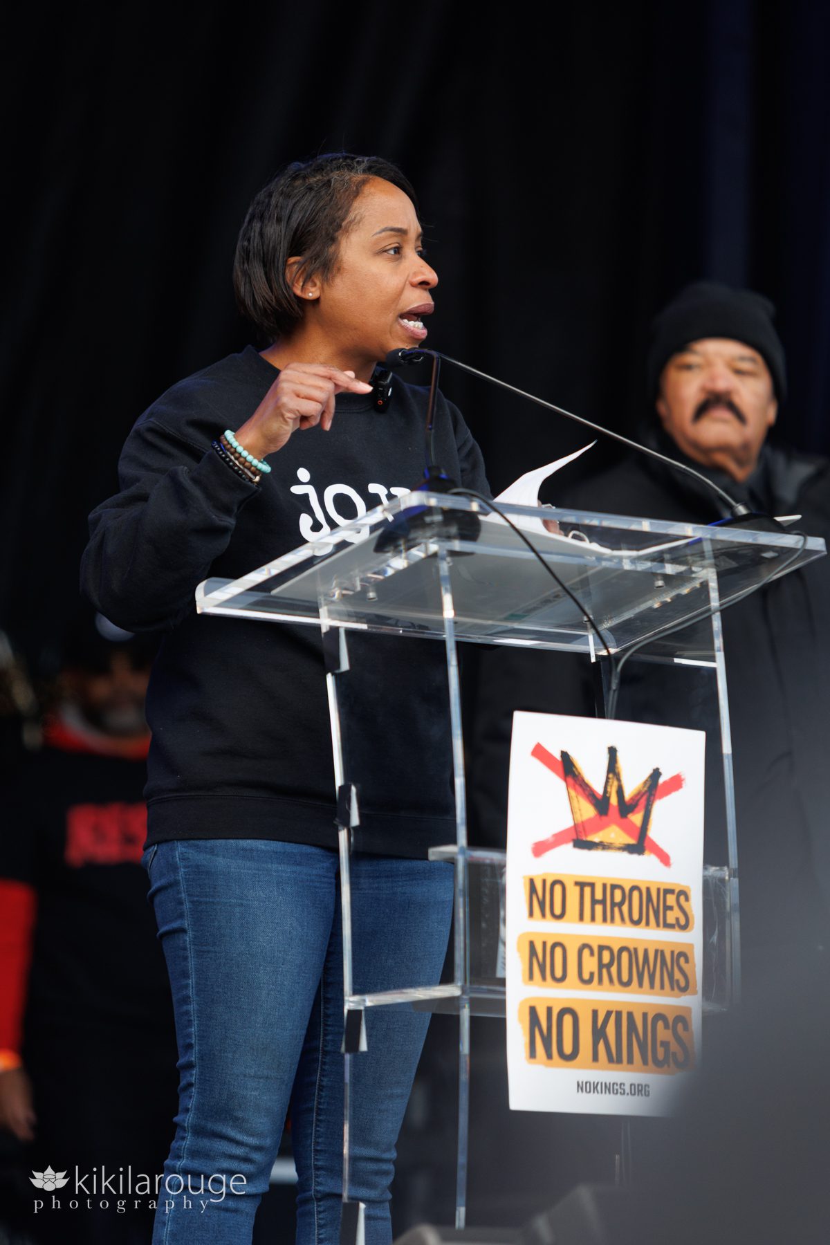 Attorney General Andrea Joy Campbell speaking on stage in a JOY sweatshirt at the Boston Common No Kings Anti Trump Protest Rally