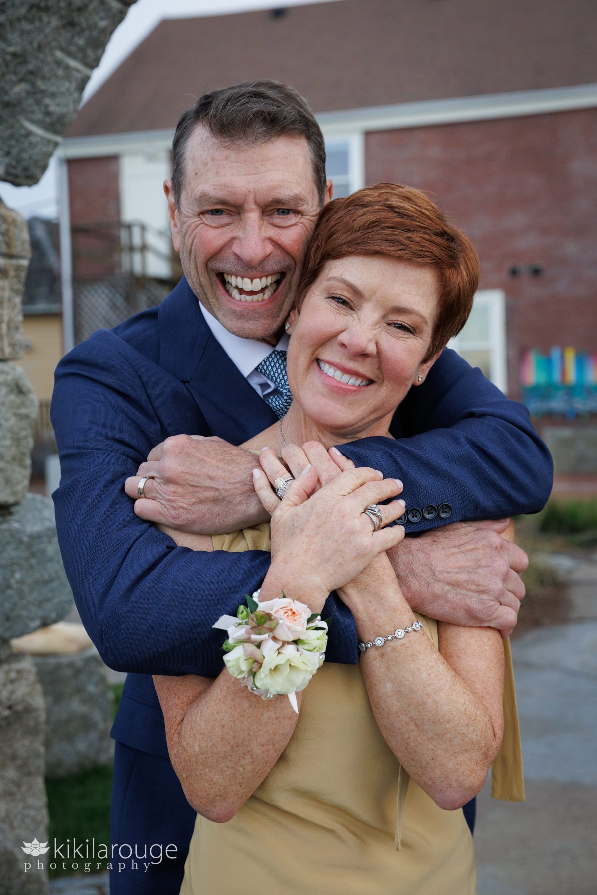Man with his arms around a redheaded woman's shoulders hugging her both smiling 