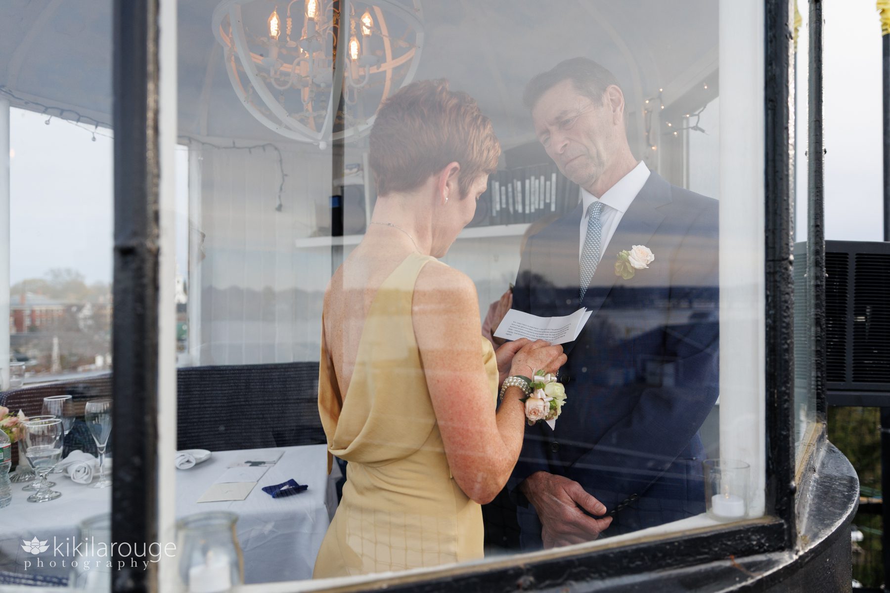 Woman with short red hair reading her wedding vows with man earnestly smiling at her at the top of a lighthouse 
