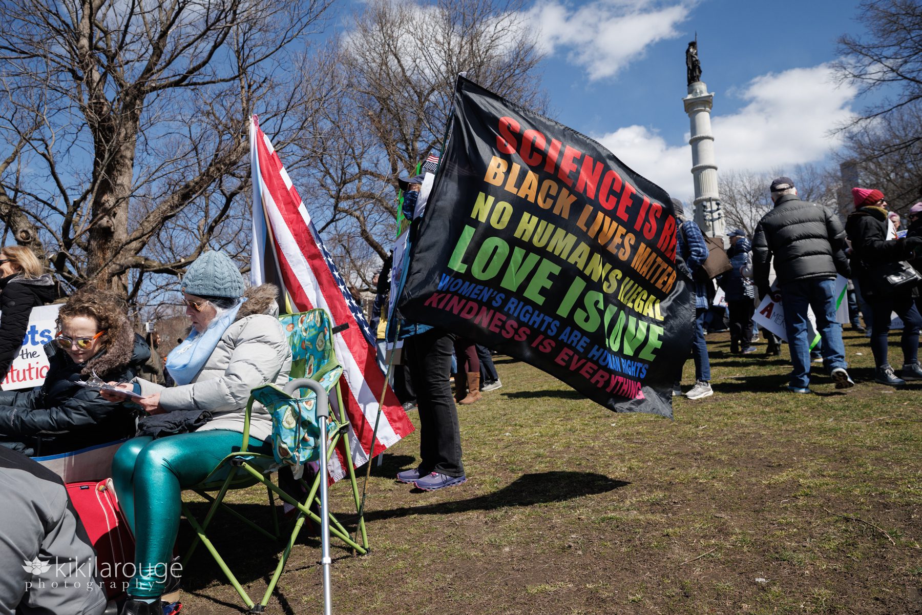 People gathered on the Boston Common in anti Trump administration protest with large black flag listing human rights