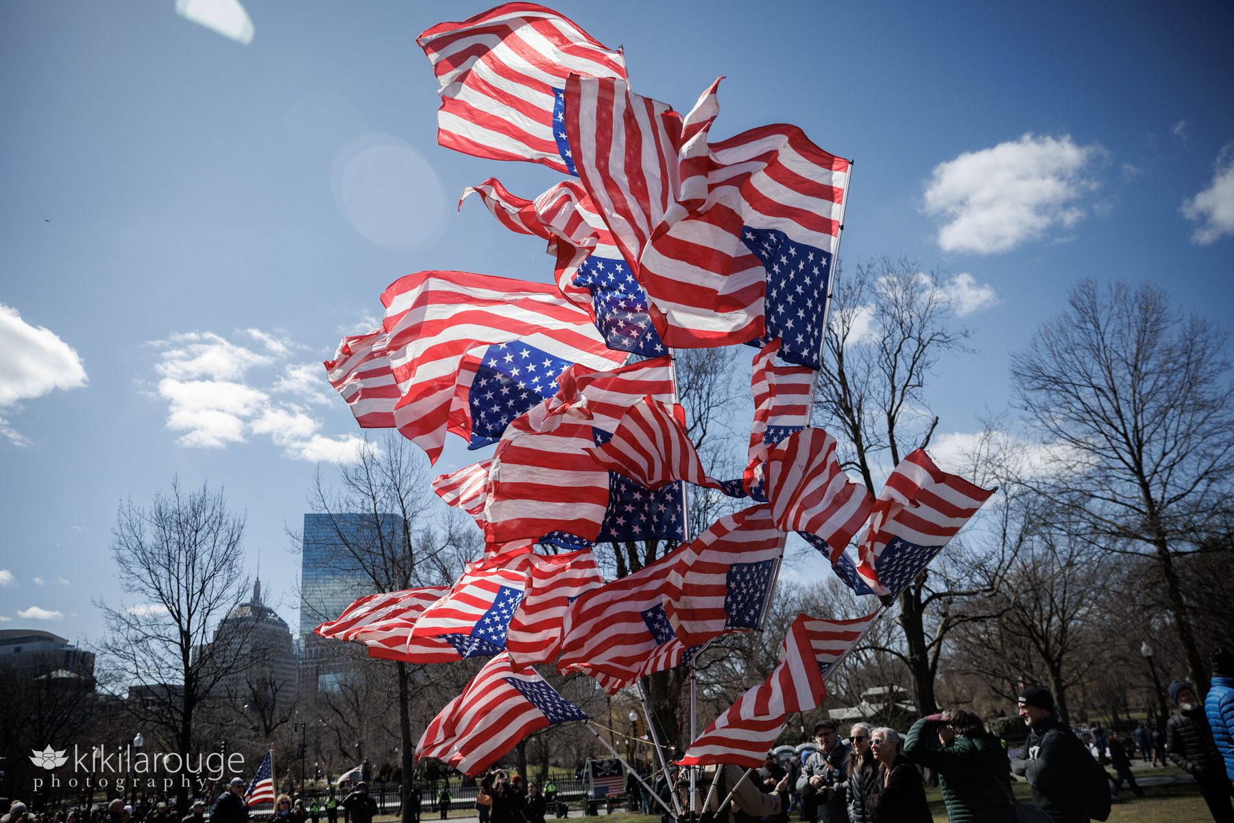 Many upside down American flags on polls attached to a man on the Boston Common with the John Hancock building in backdrop No Kings 3.0