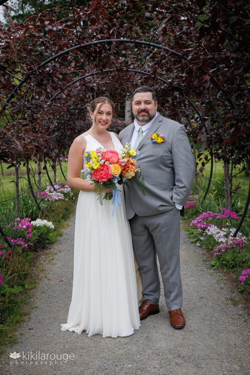 Wedding couple in garden with black metal circular arches covered in leaves and flowers in bloom
