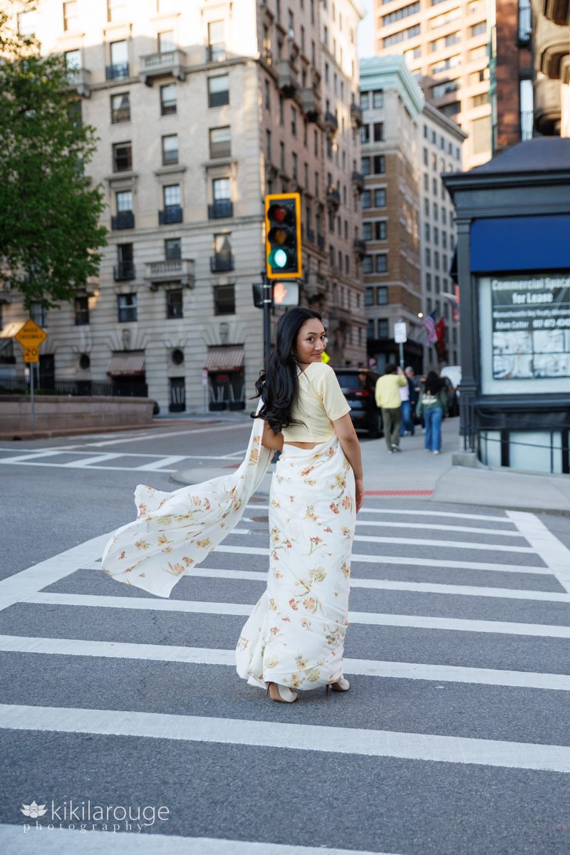 Girl walking in crosswalk on Beacon Street in Boston with green light looking back at camera and pretty sari blowing in the wind