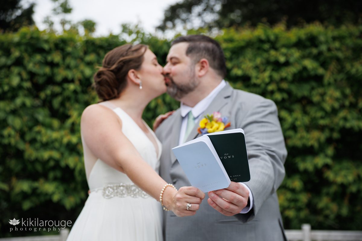Close up in focus two wedding vow booklets for bride and groom and they are kissing out of focus in back drop