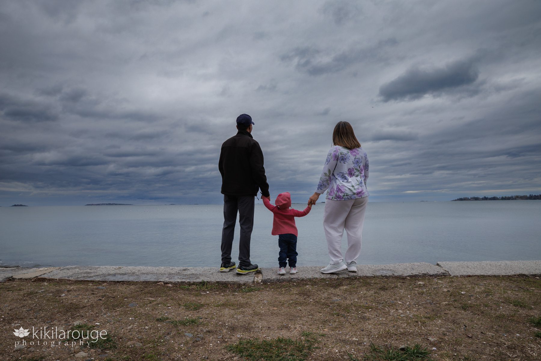 Couple standing on ledge at beach with dramatic skies looking out onto the ocean