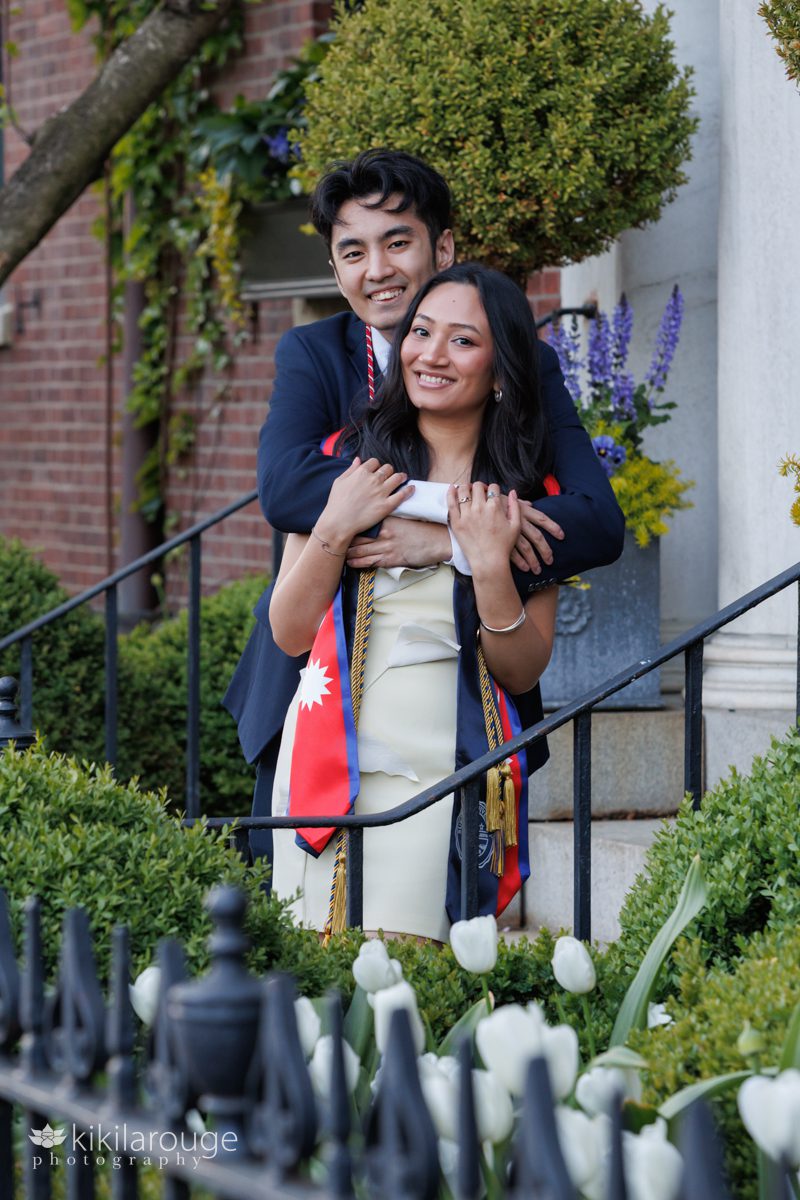 Cute young Nepali couple hugging on steps of home on Beacon Street surrounded by Boston's spring blooms including white tulips