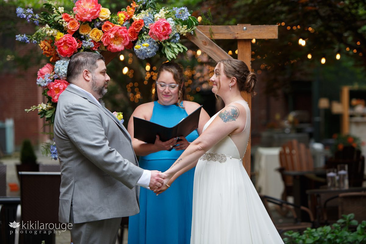 Wedding couple at wood altar adorned with beautiful colorful flowers and women in turquoise blue dress officiating the ceremony 