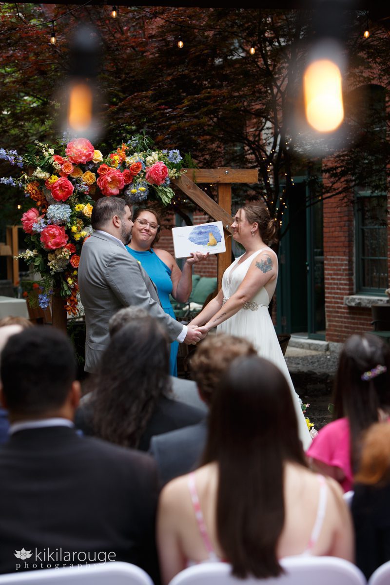 Couple at altar and officiant holding up and reading a book about love