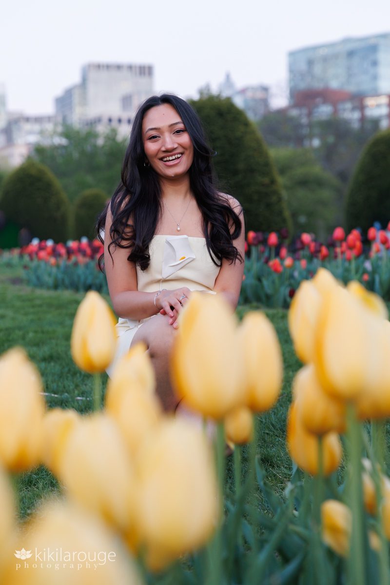 Woman surrounded by colorful tulips on Boston Common wearing a pale yellow dress with white flowers on it smiling 