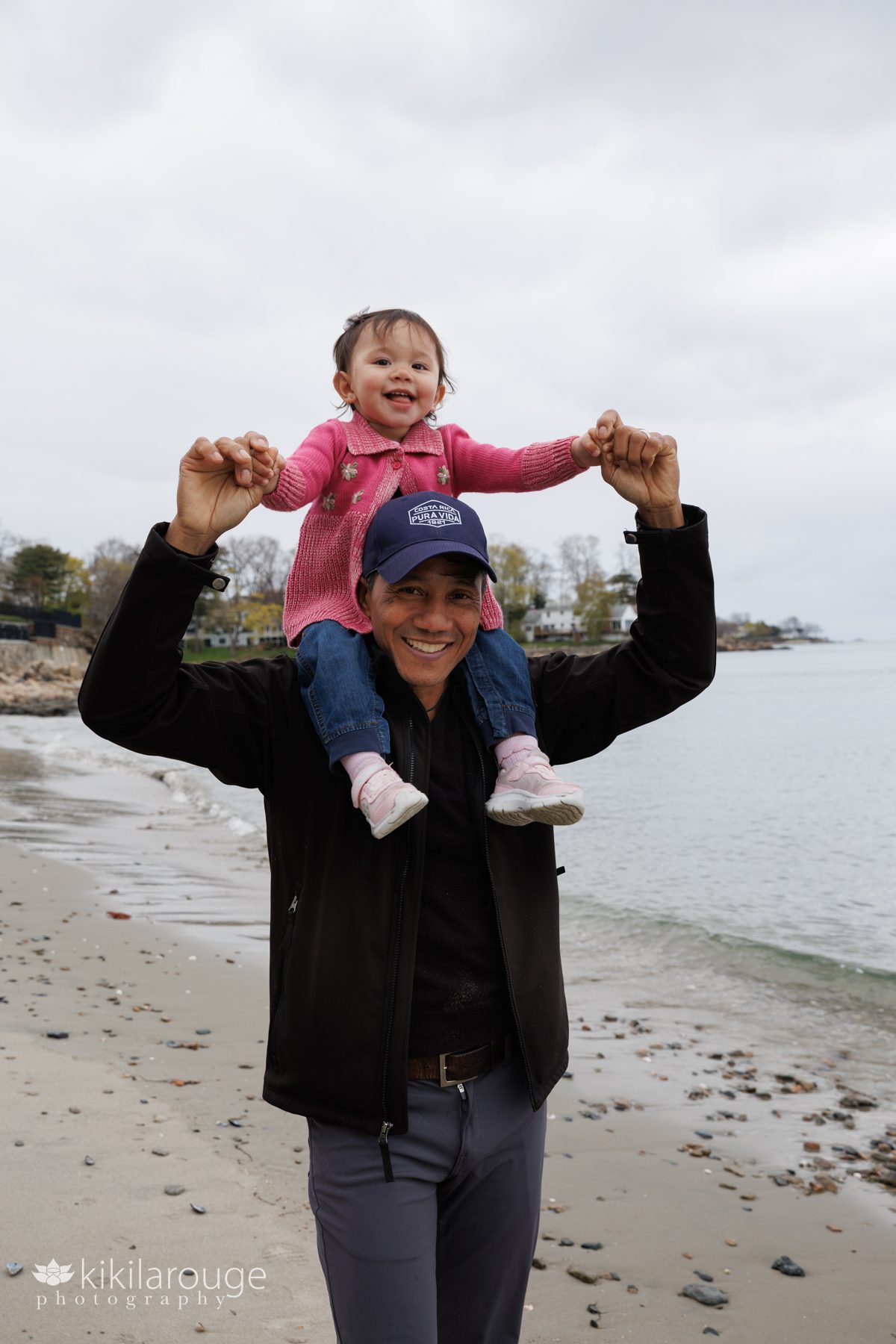 Little toddler girl in pink on her dad's shoulders at the beach