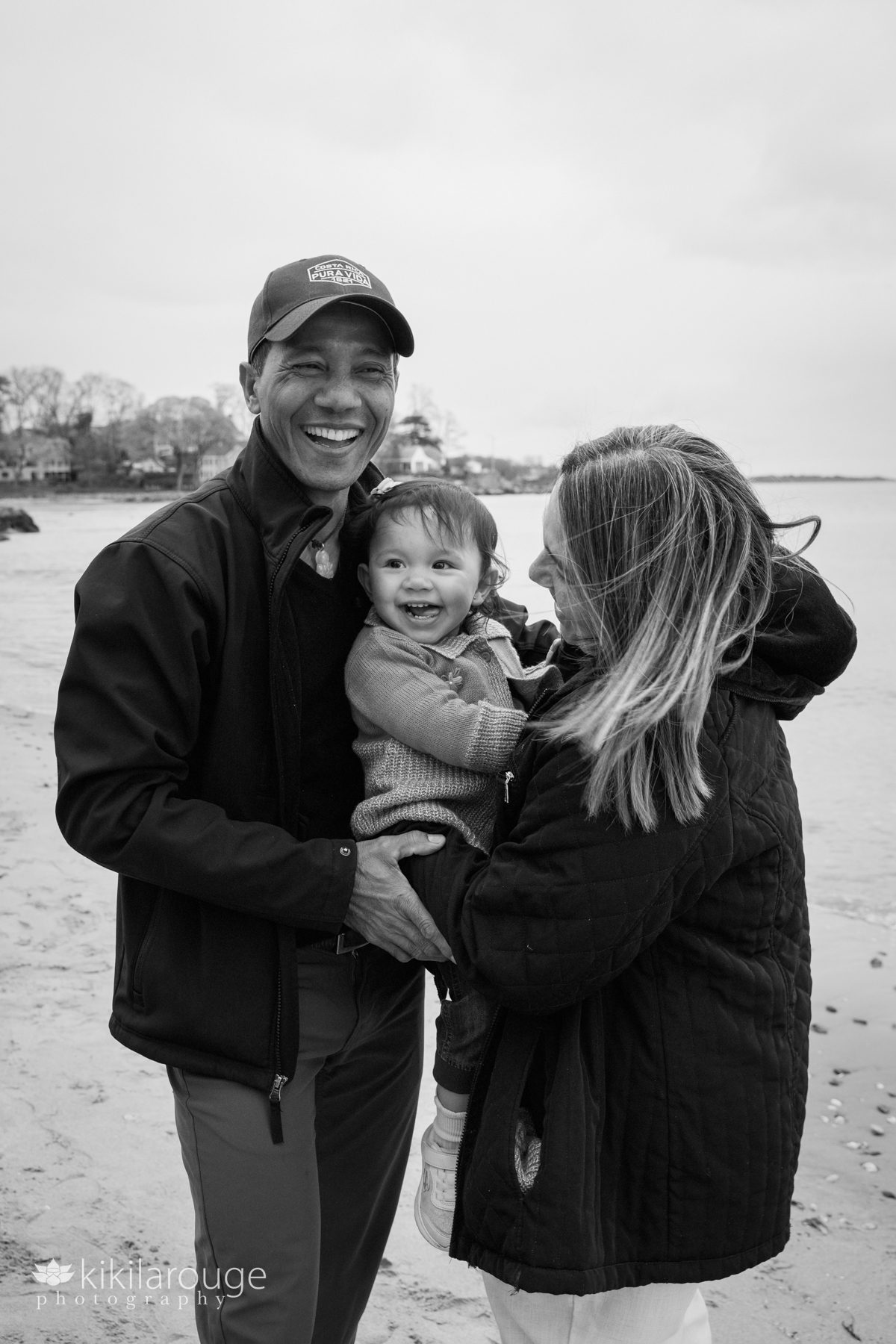 Little girl laughing being held in between her parents at the beach