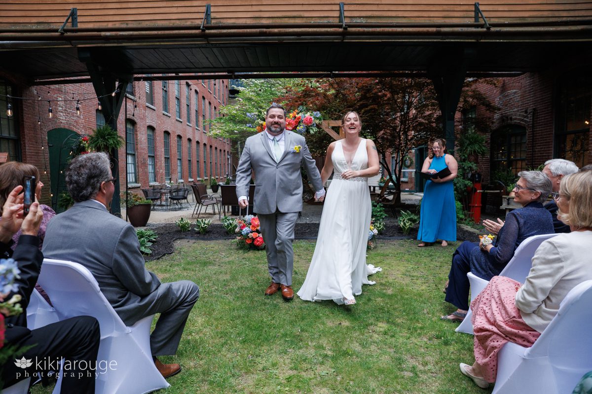 Wedding couple smiling and walking back up the aisle after the ceremony with guests looking on