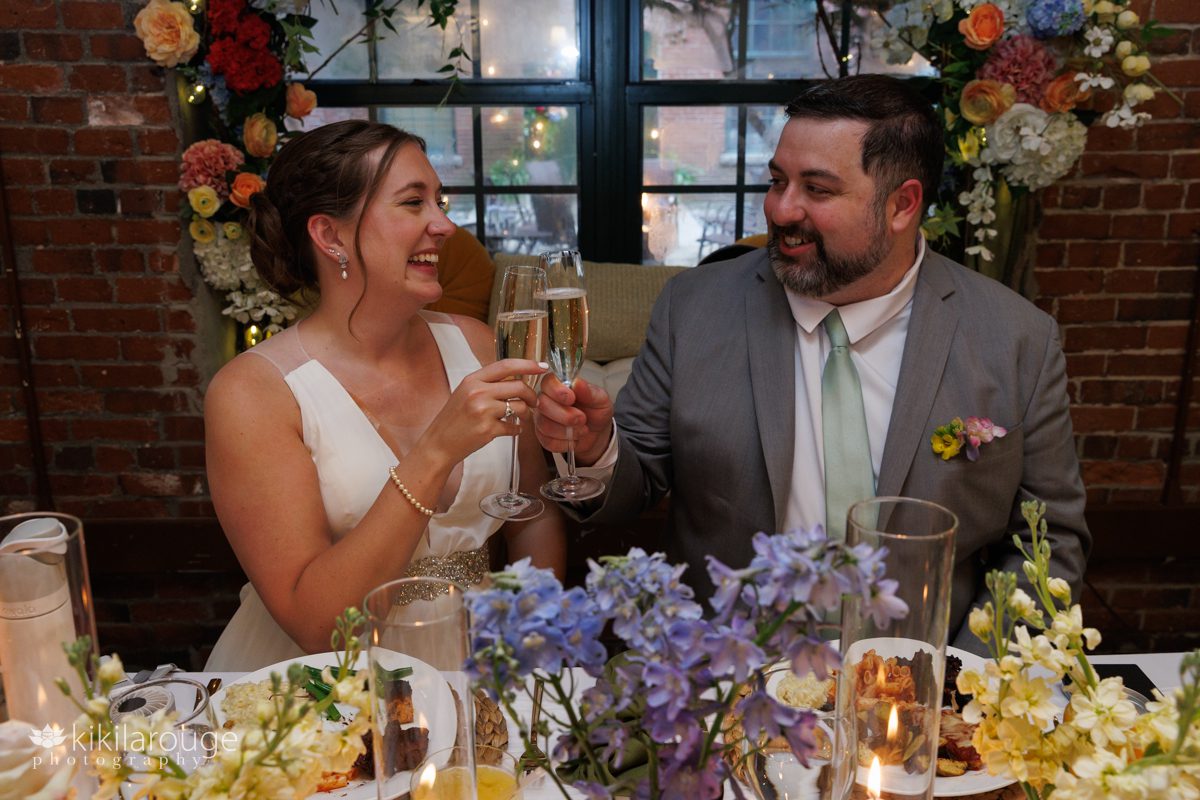 Couple at their wedding sweetheart table toasting with champagne