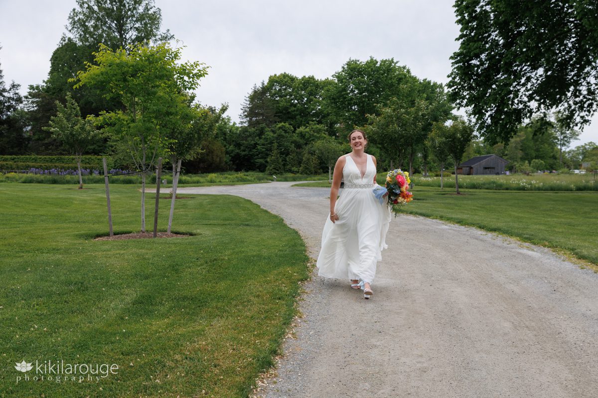 Bride smiling and walking towards camera in beautiful green park holding vibrant bouquet