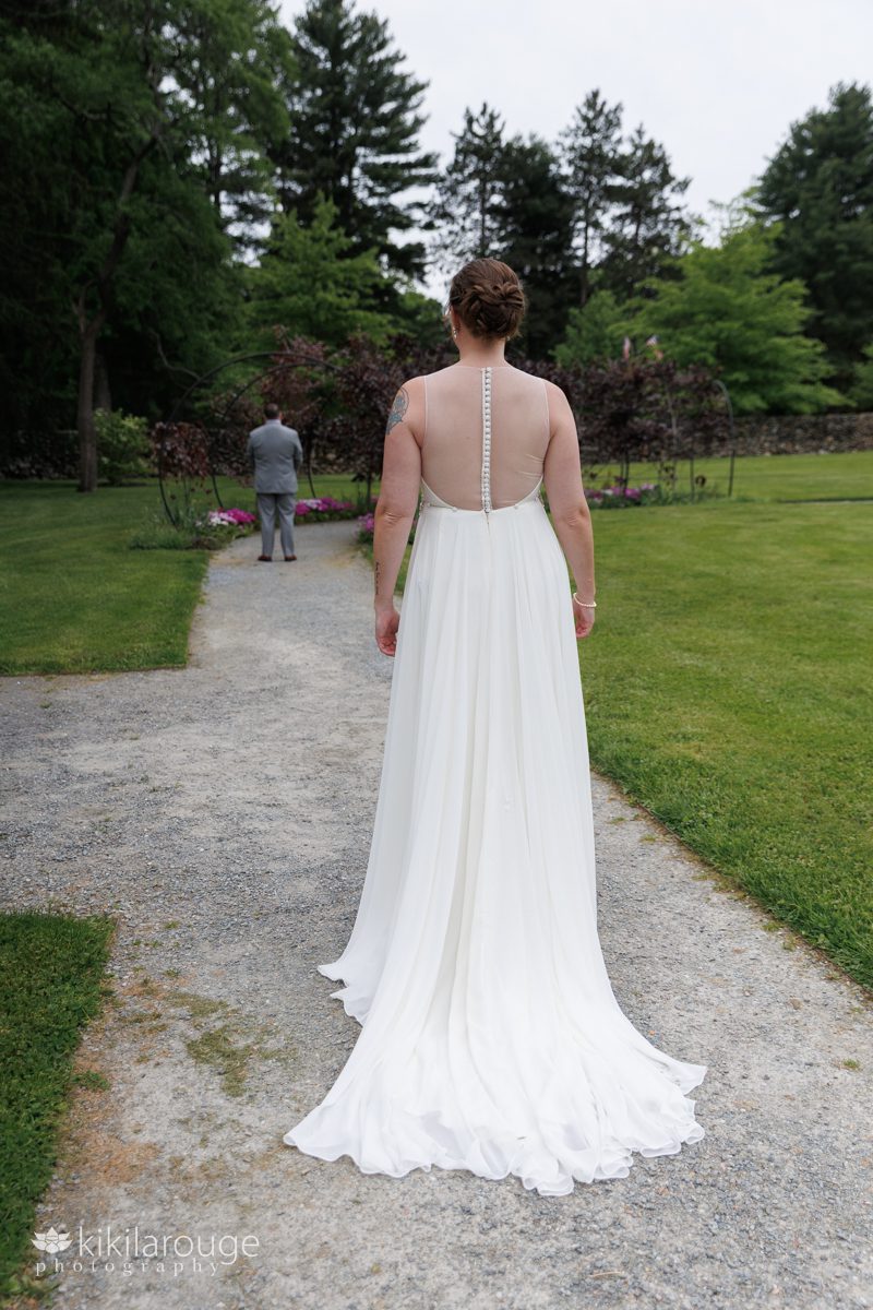 Bride's back walking towards groom waiting in the distance in beautiful Stevens Coolidge gardens in gray suit