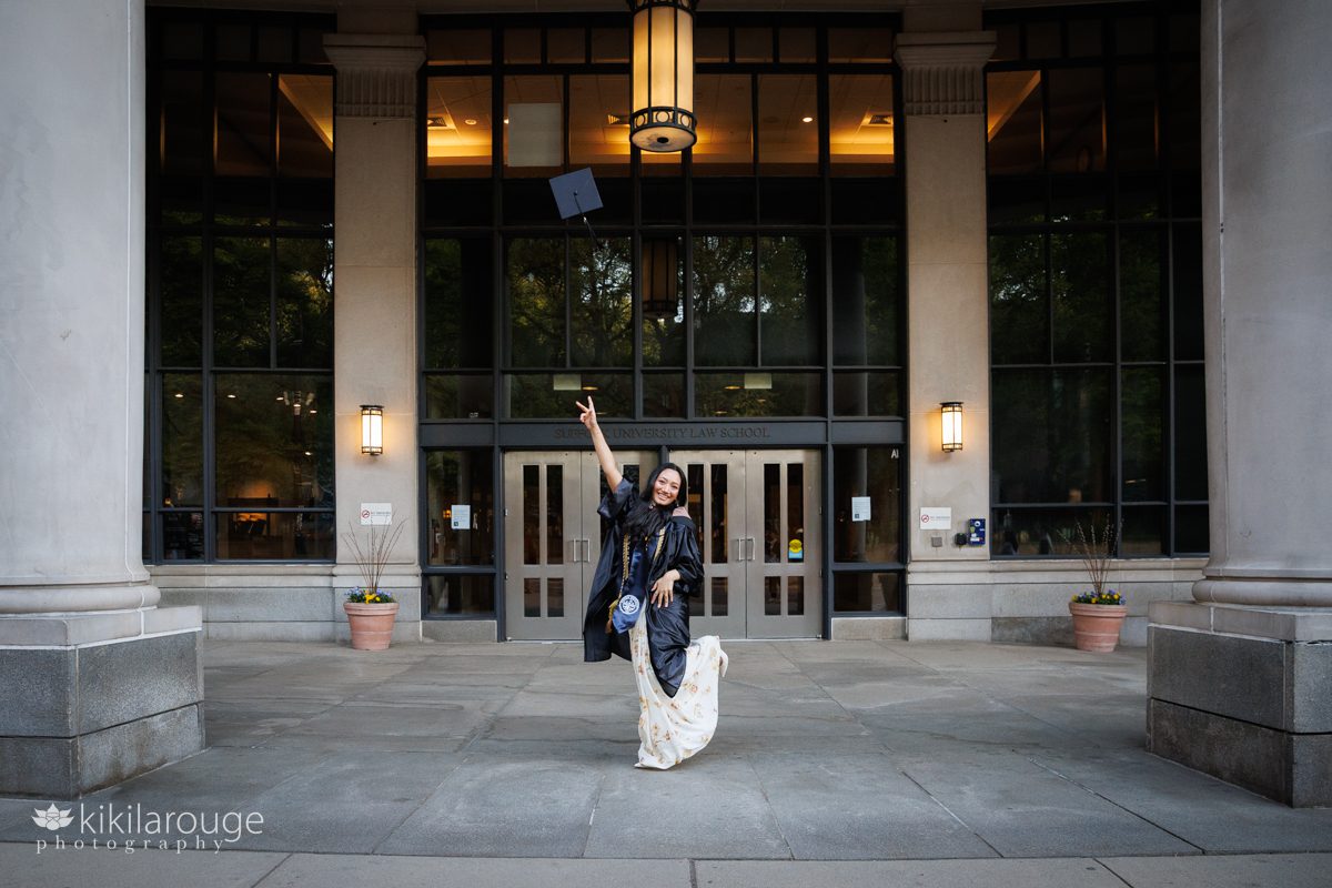 College graduate throwing her cap up into the air with her leg kicked up and big smile in front of Suffolk University Law School building in Boston MA