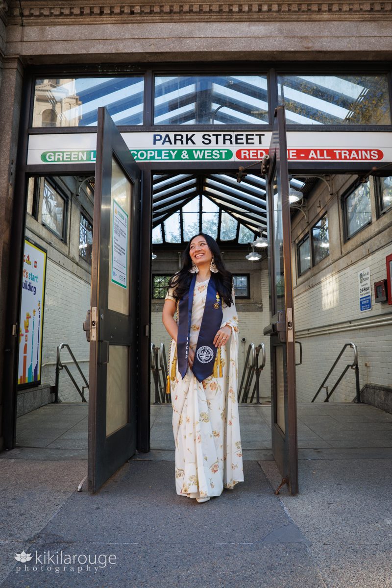 Beautiful young woman with long black hair in yellow floral sari and Suffolk University graduation stole in front of the MBTA Park Street entrance on Boston Common