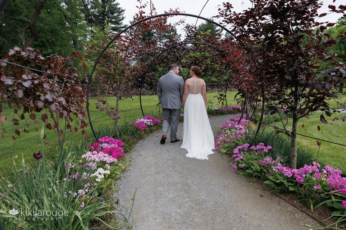 Wedding couple walking through circular metal archway in beautiful garden with flowers in bloom
