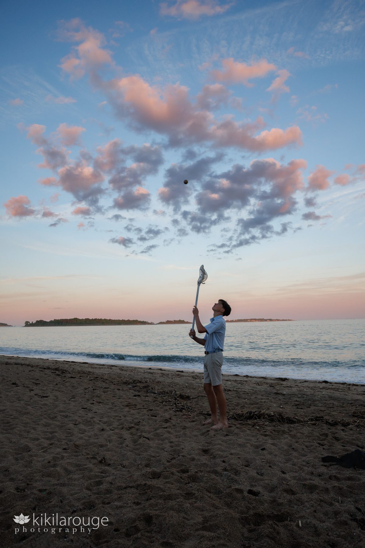 Boy playing with lacrosse stick and ball on beach with dramatic sunset