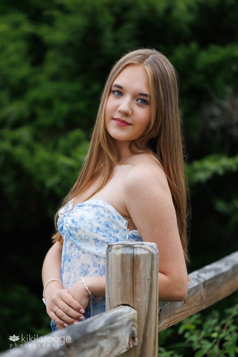Senior portrait girl in blue and white top leaning on wooden fence