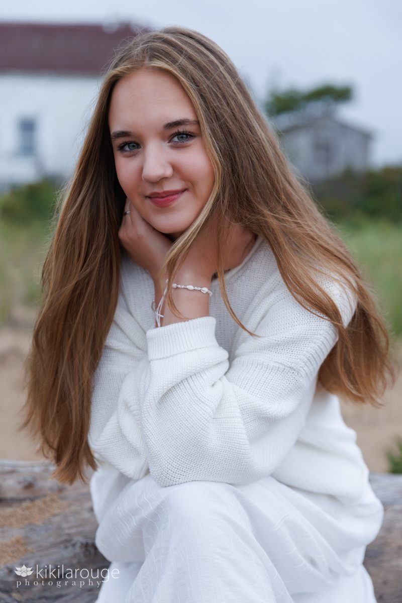 Portrait of a teen girl sitting on driftwood at beach in white sweater and long dress
