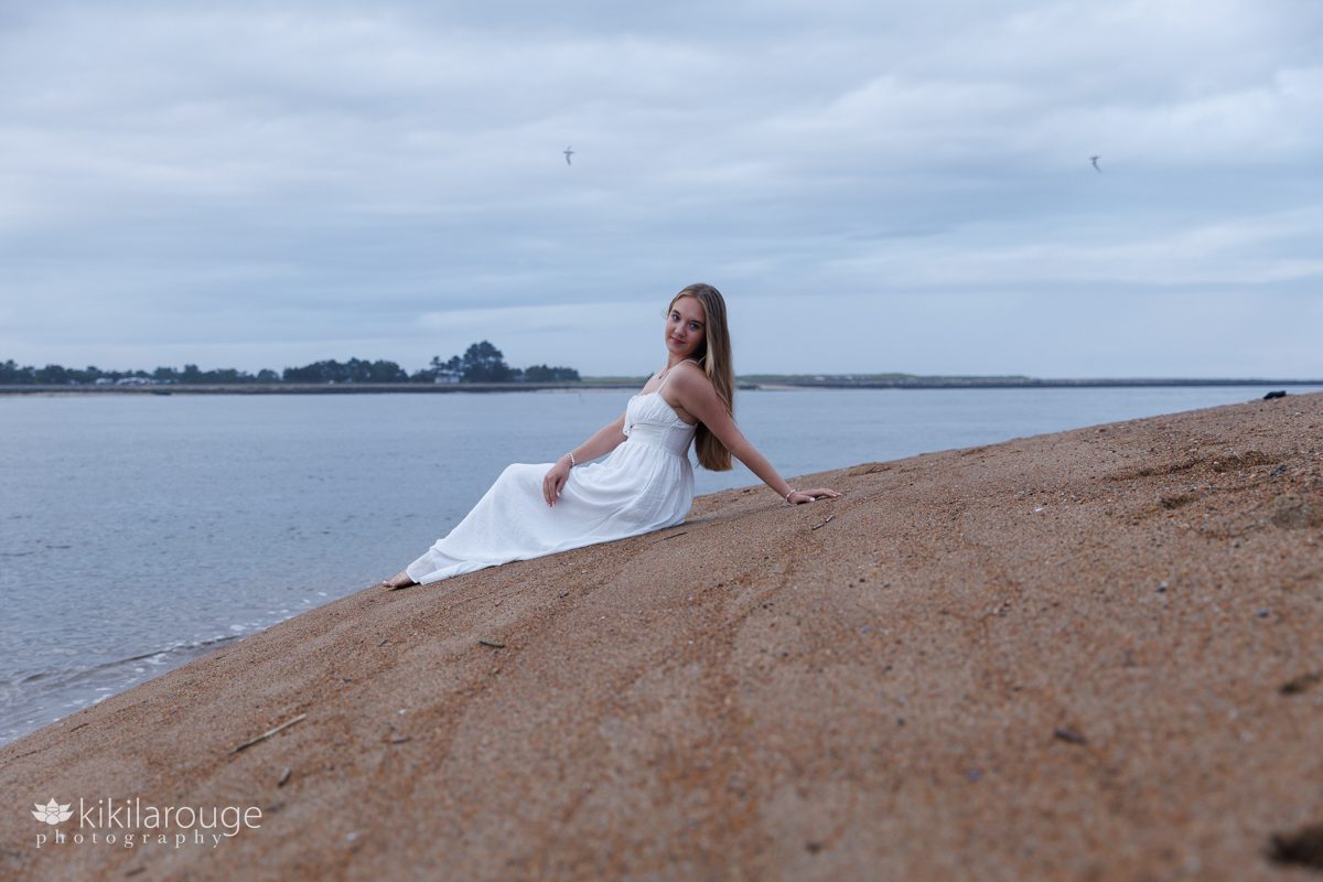Girl sitting on beach in long white summer dress 
