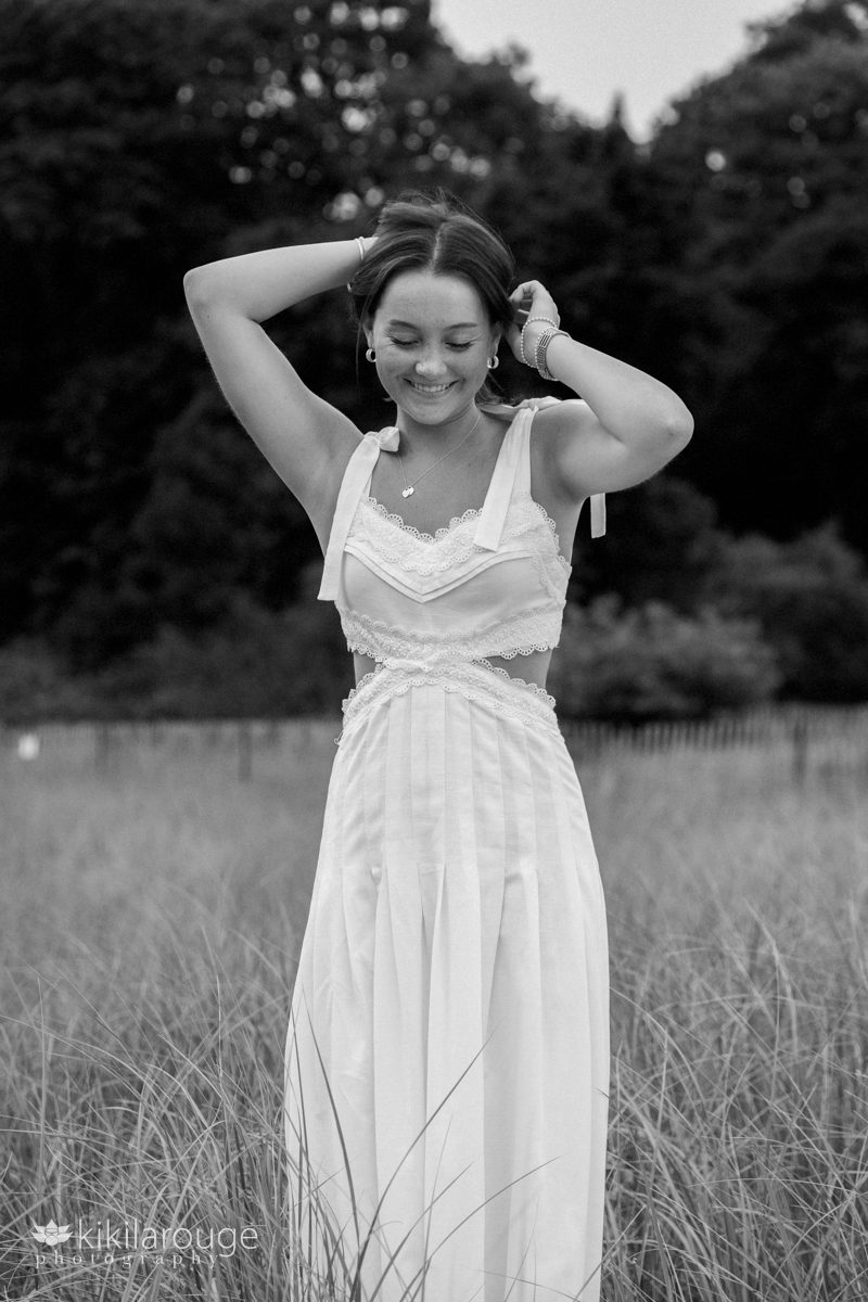 BW of brunette teen girl walking in beach dunes in a Lacey white summer dress with her hands in her hair