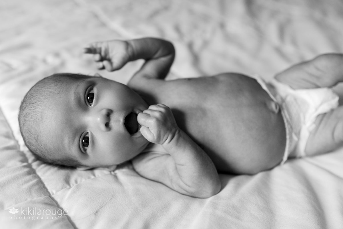 Naked newborn baby in diapers looking at camera with hand in her mouth