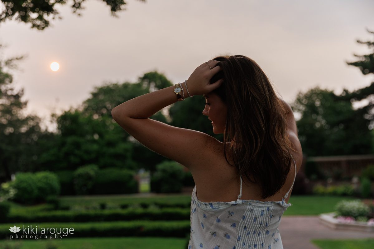 Silhouette of teen girl with hands on her head standing by garden with hazy sun 