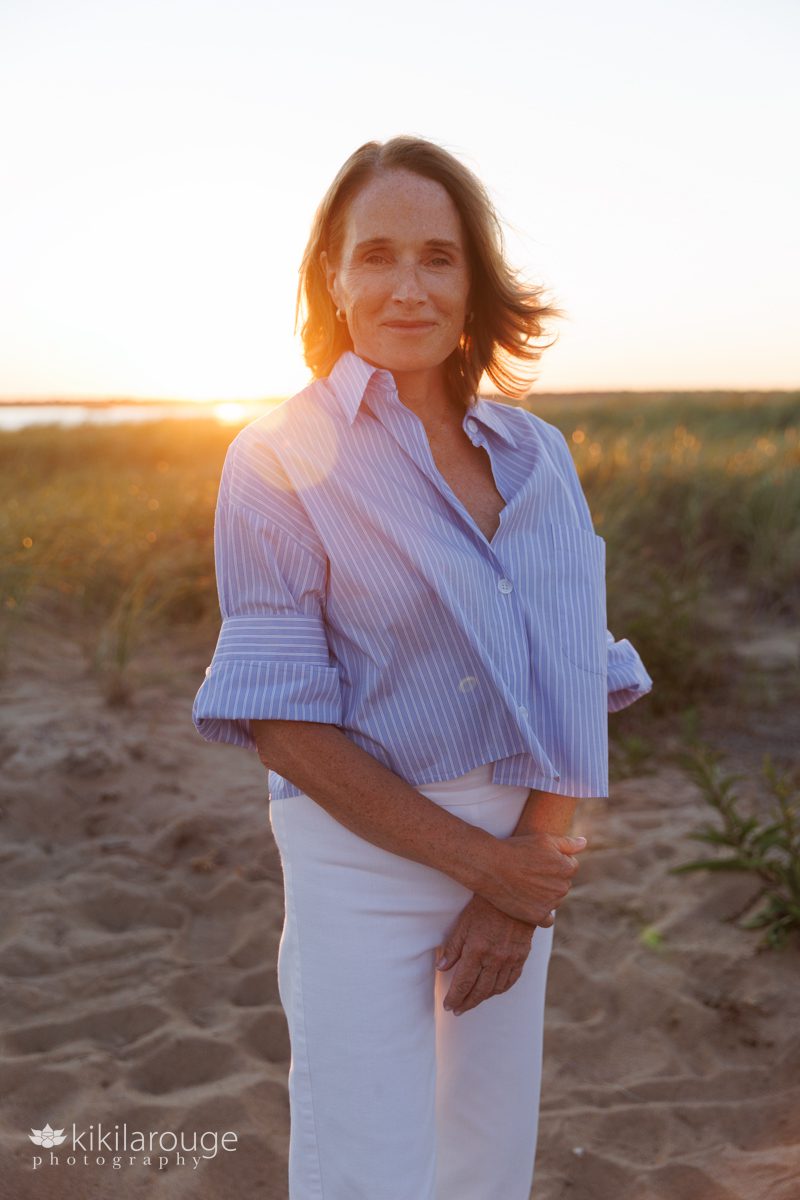 Woman with blonde hair standing in sand dunes with orange bright sun flare