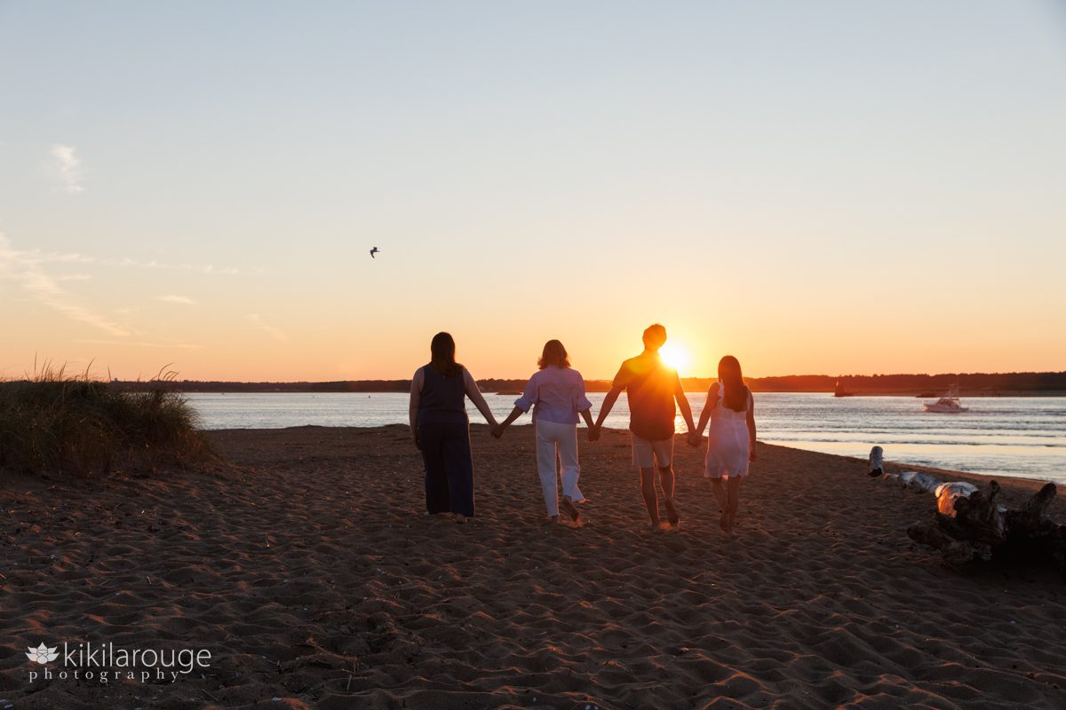 Family of four walking down beach towards the sunset with a flare and driftwood and boat