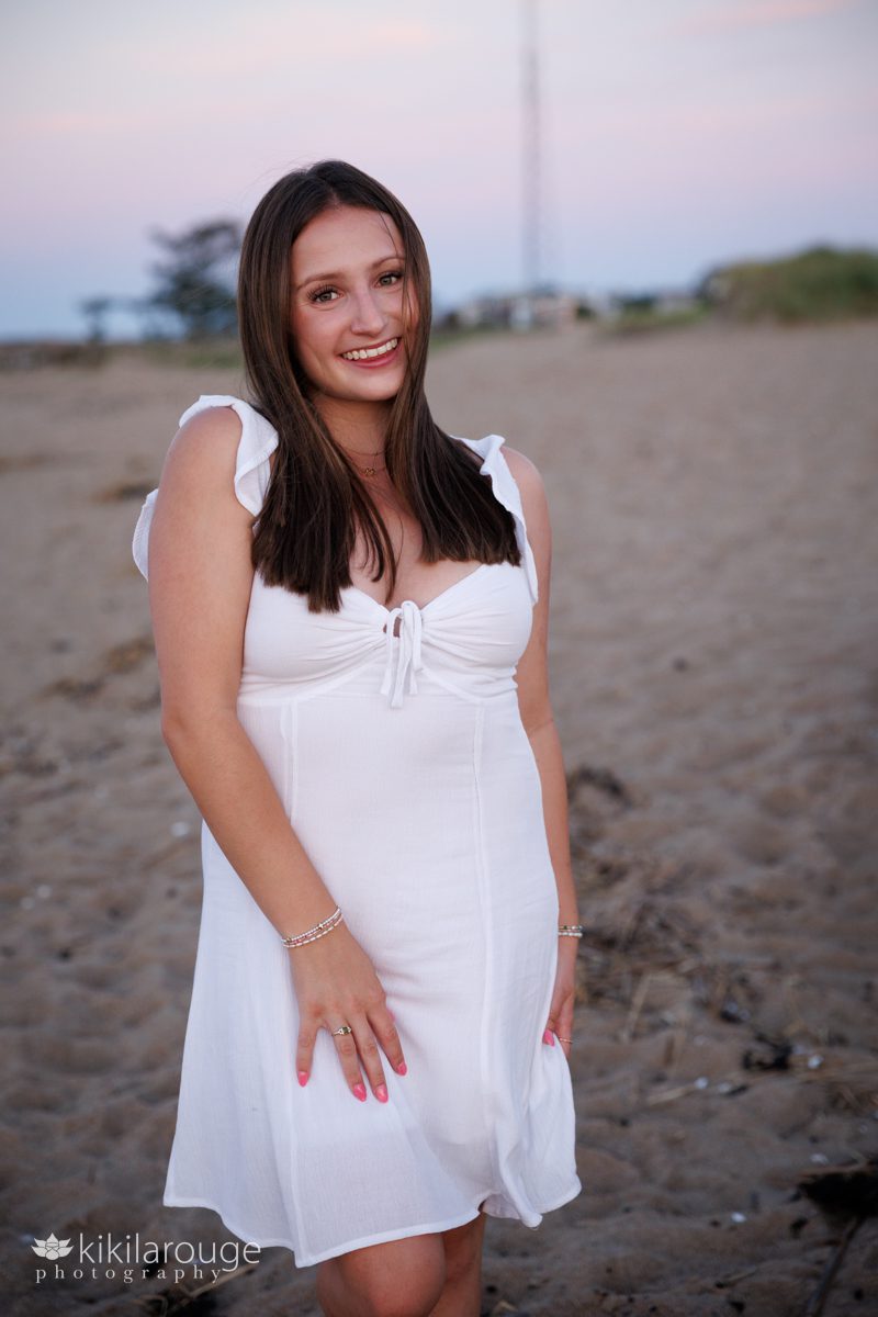 Young woman in white sun dress smiling on the beach at sunset