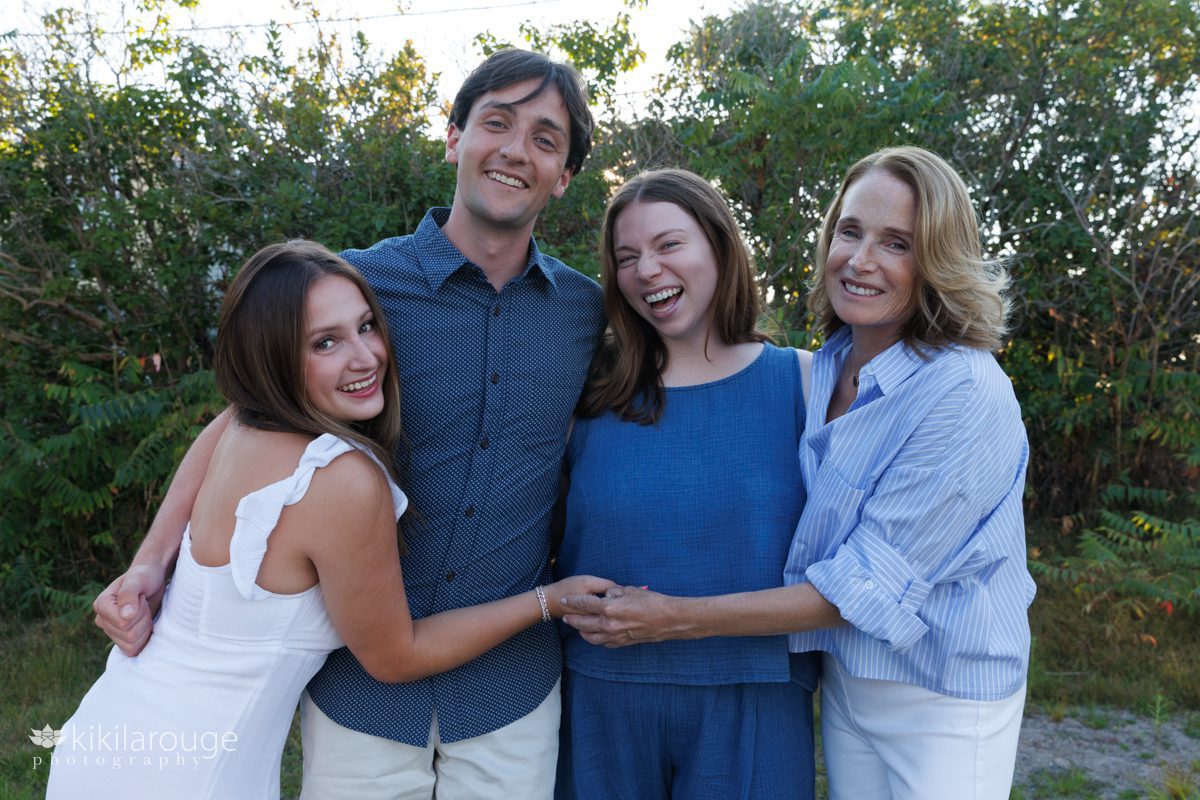 Portrait of a Mom with her three 20 something kid hugging and smiling with sunlight back and greenery backdrop