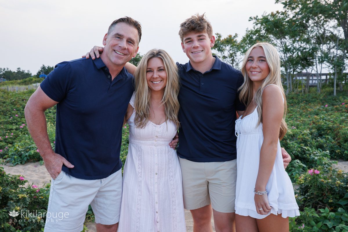 Family portrait of Mom and Dad with their two High School Seniors a boy and girl dressed in navy blue, white and pinks and beach roses in backdrop