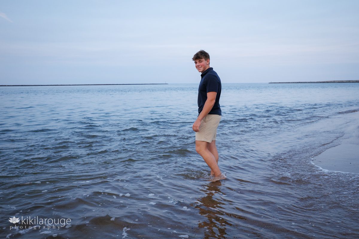Senior boy with khaki shorts and navy blue shirt walking into the water at Plum Island beach