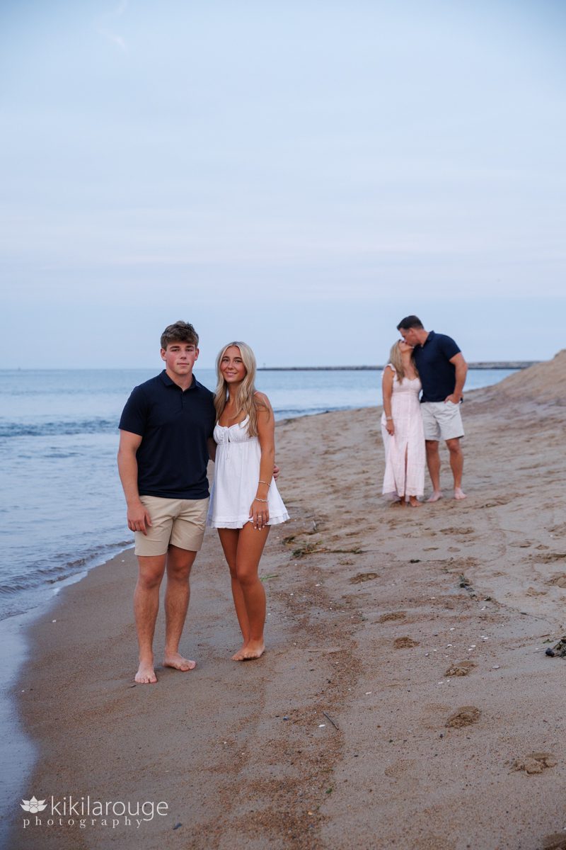 Teen siblings tougher and Mom and Dad in Backdrop out of focusing kissing along the shoreline at the water's edge on Plum Island