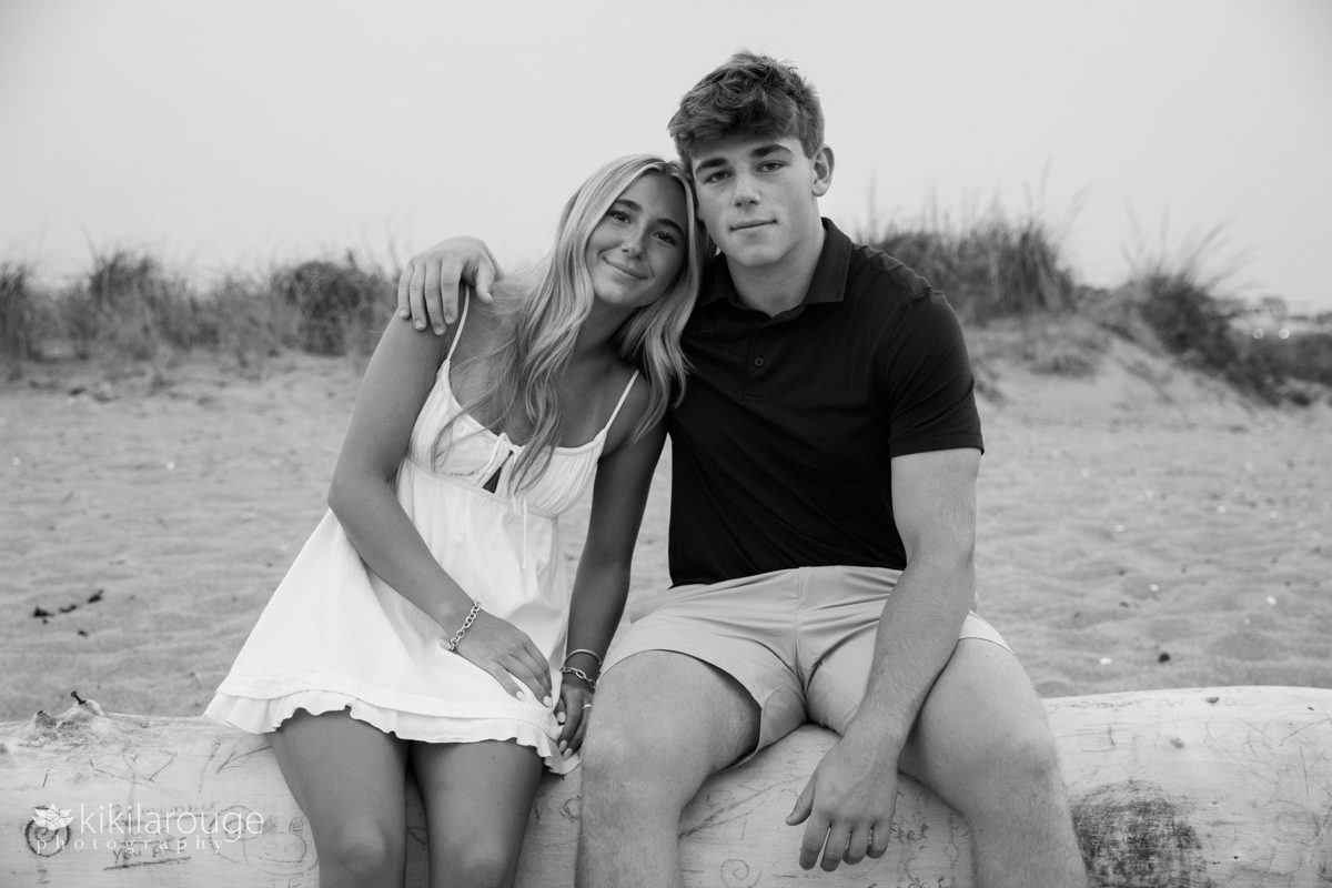 BW of Senior siblings boy and girl sitting on large driftwood at the beach on Plum Island
