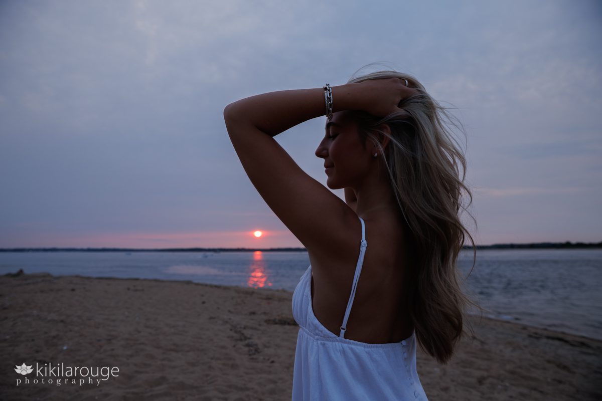 Silhouette of a teen girl in white dress with long blonde hair and a pink sun setting on the horizon in the backdrop