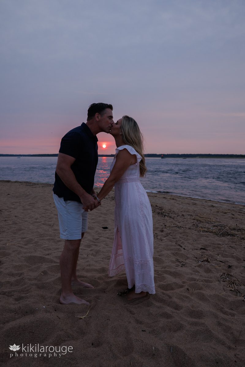 A couple in silhouette kissing with the sunsetting in backdrop between them
