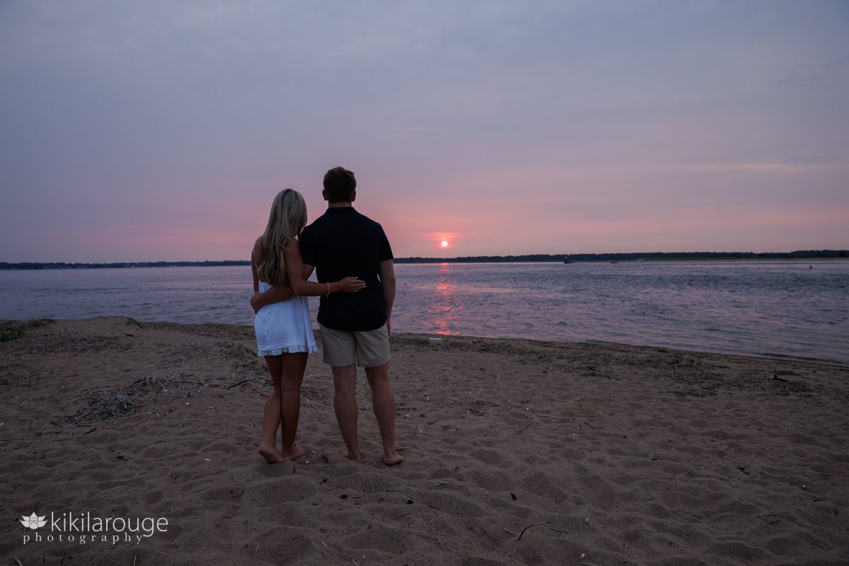 Sibling Seniors boy and a girl arm and arm in silhouette looking out at the pink sunset on Plum Island