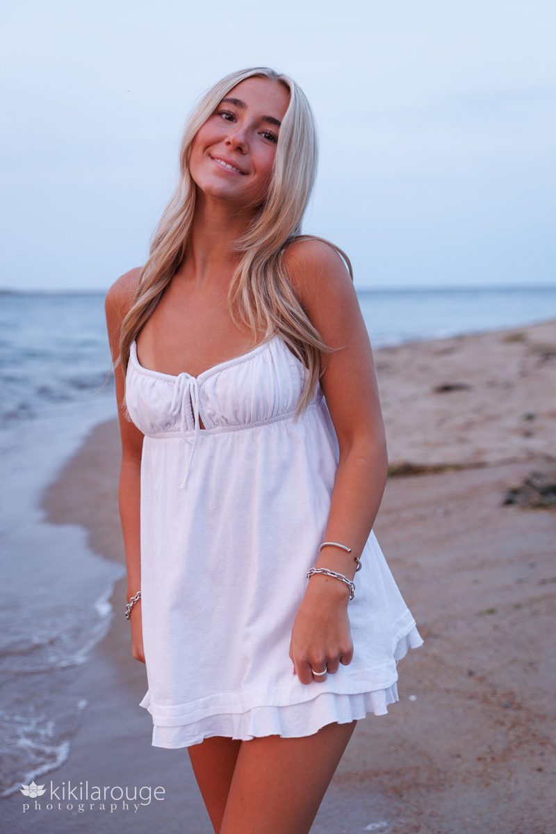 Teen girl senior portrait in short white sundress and long blonde hair at the water's edge