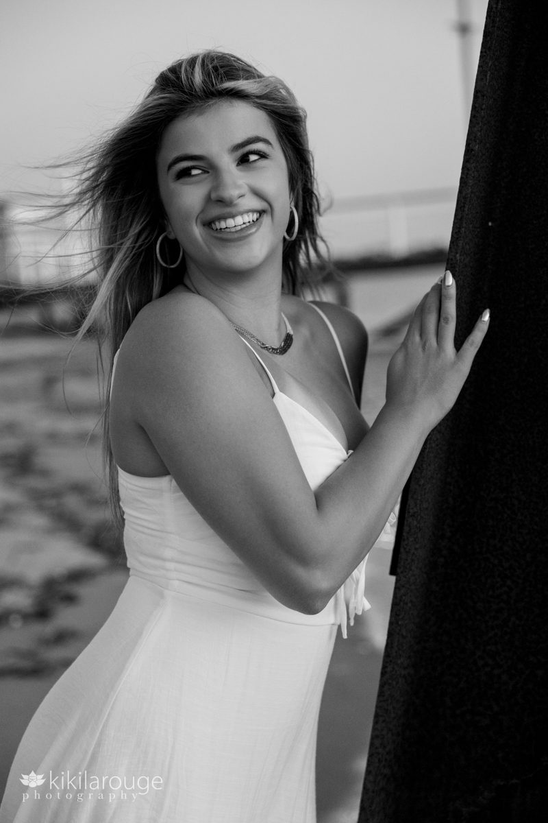 Black and white photo of teen girl leaning on metal ballast at Plum Island looking of to side laughing