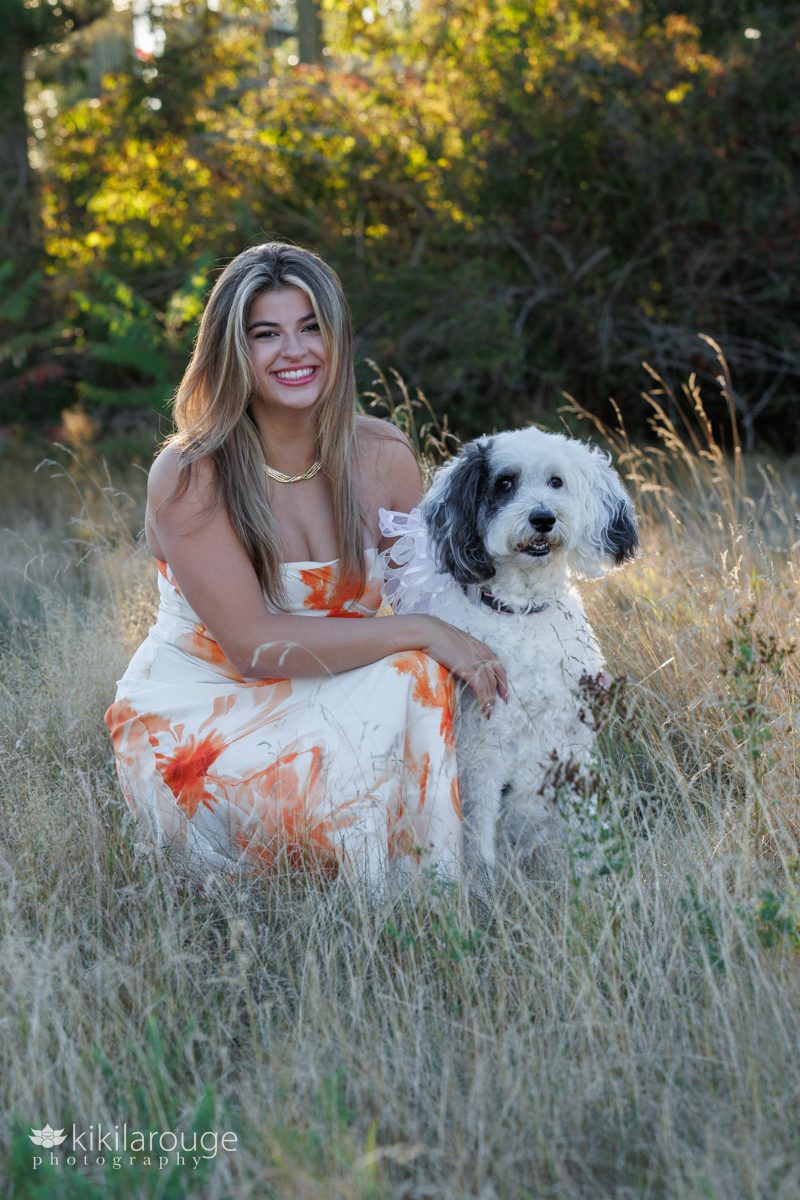 Senior girl in beach reeds in long orange and white dress with black and white doodle dog