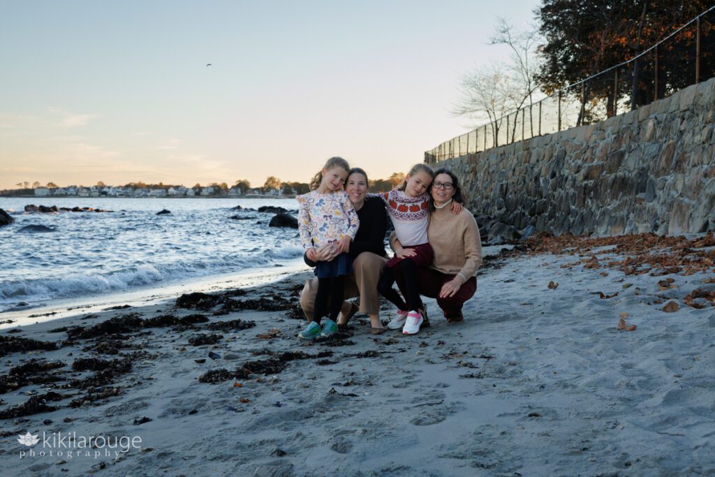 Family of four with two Moms and seven and six year old daughters all together on the beach at sunset with waves on the side